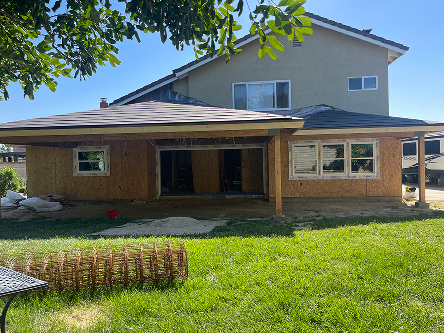 Backyard with a home under construction, tan siding, green grass, and blue sky.