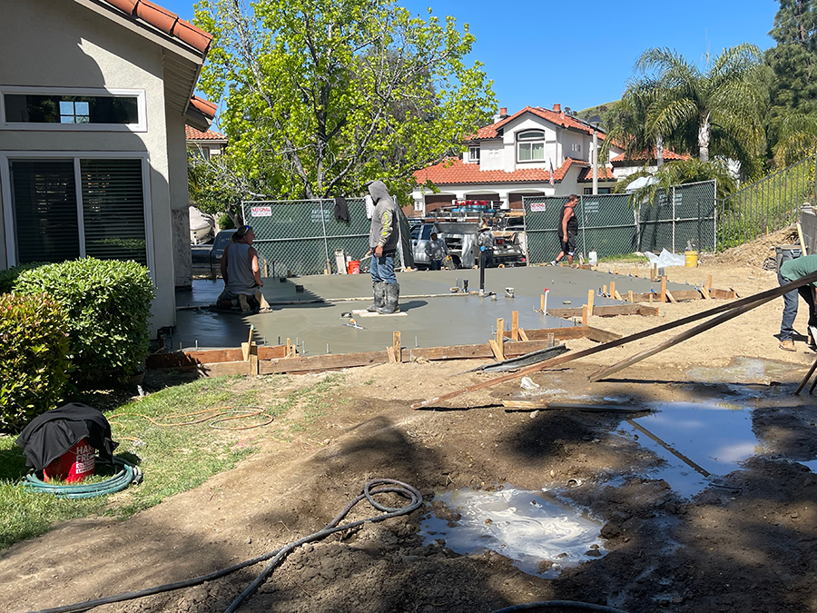 Construction workers pouring concrete for a driveway; residential setting.