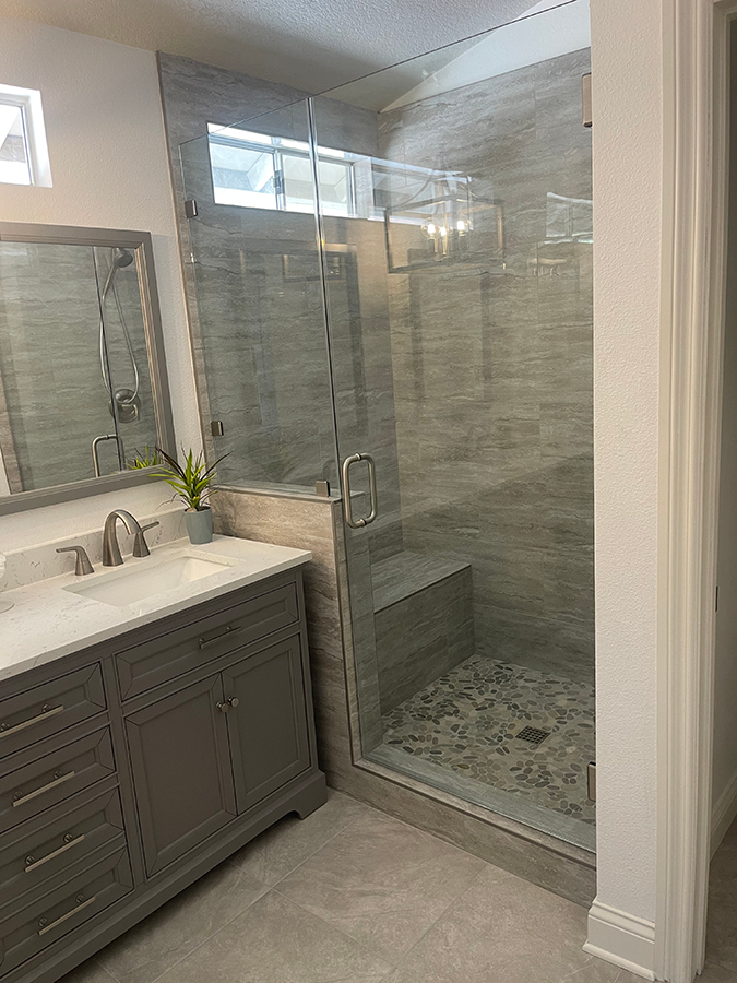 Gray bathroom with glass shower, vanity, and stone tile floor.