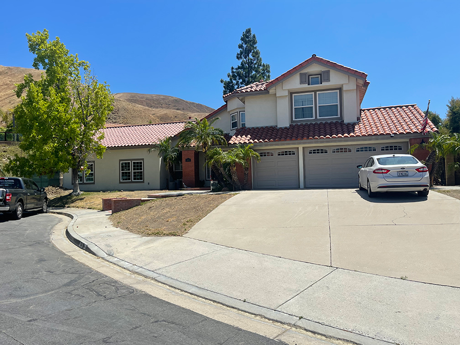 Two-story house with red tile roof, garage, and driveway; a car is parked in front. Sunny day.
