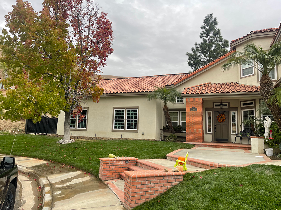 House with red tile roof, green lawn, and trees under a cloudy sky.