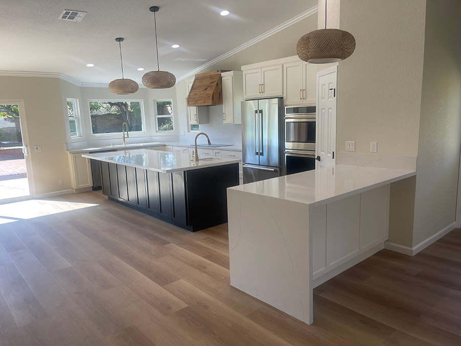 Modern kitchen with island and bar; white and black cabinets, stainless steel appliances, hardwood floor.