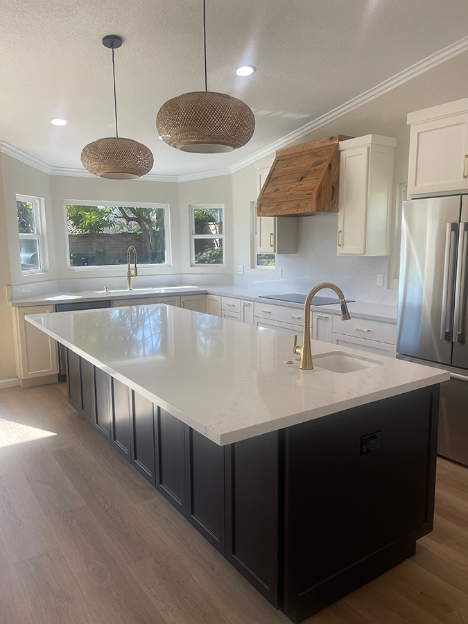 Modern kitchen with large island, white countertops, dark cabinets, light wood floors, and woven pendant lights.