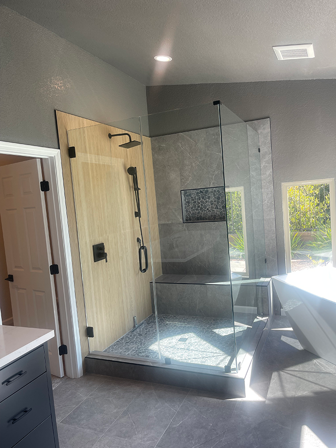 Modern bathroom with glass shower, light wood walls, and black fixtures.