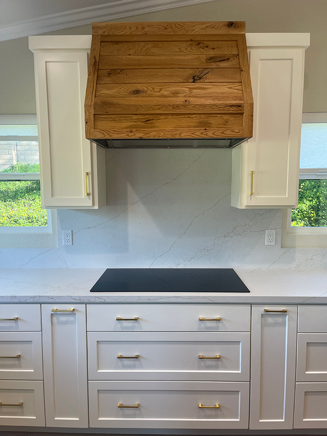Kitchen with white cabinets, quartz countertop, and a wooden range hood over a black cooktop.