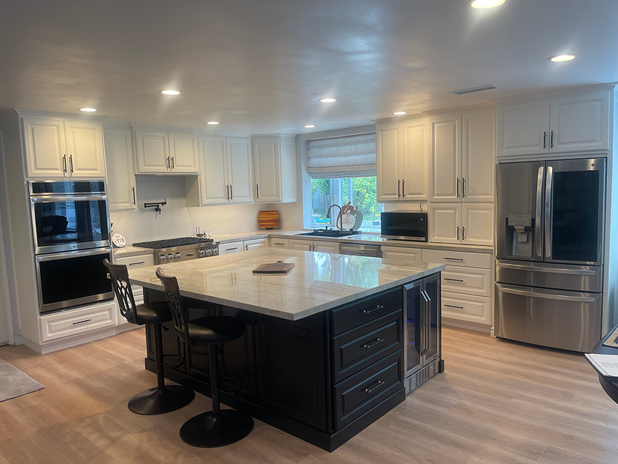 Spacious white kitchen with a black island, stainless steel appliances, and light wooden floors.