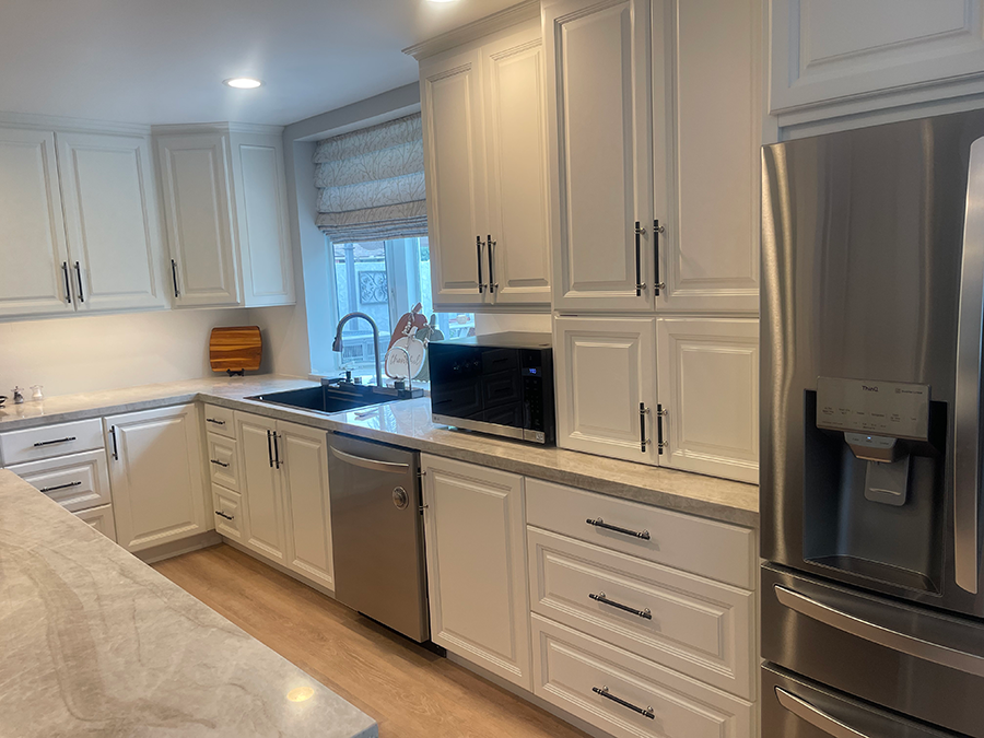 White kitchen with stainless steel appliances, light countertops, and wood-look flooring.