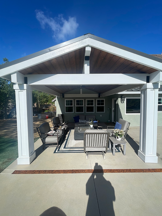 Outdoor patio with a covered seating area, blue sky, and various gray furniture.