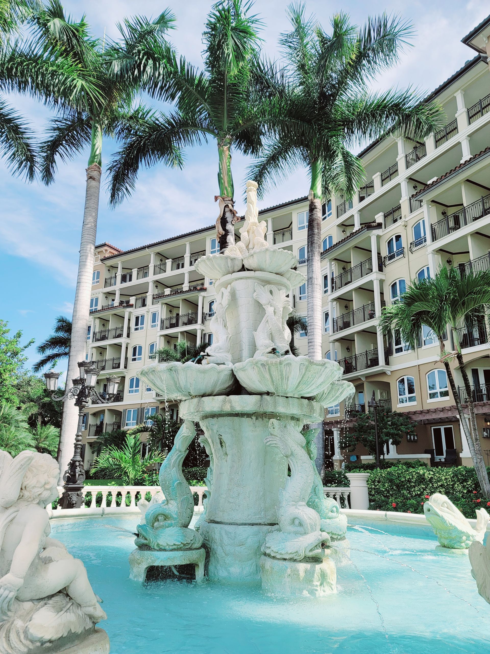 Tiered fountain in a courtyard with palm trees and an apartment building in the background