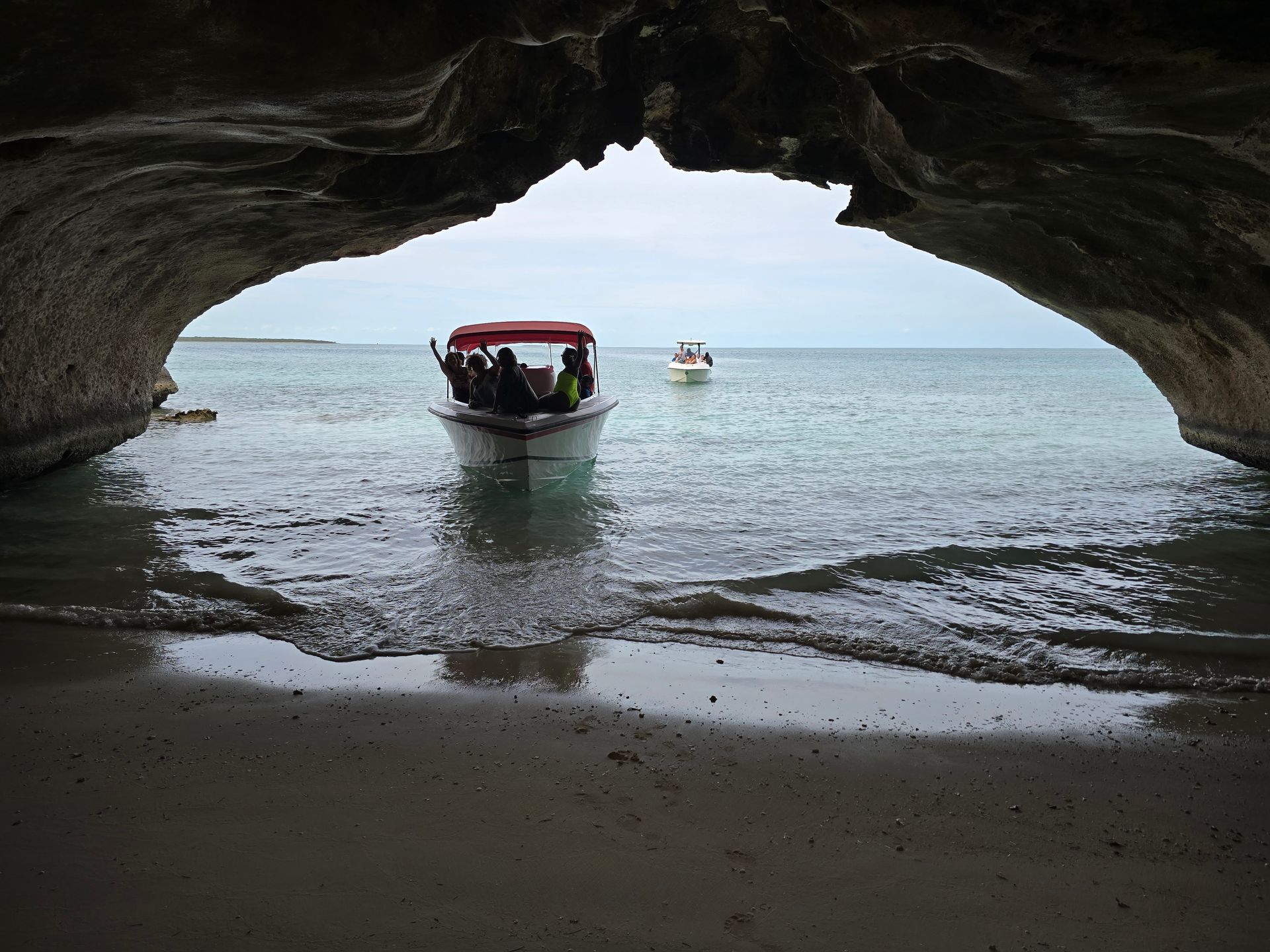 People in a small boat on calm sea, viewed from inside a rocky cave opening.