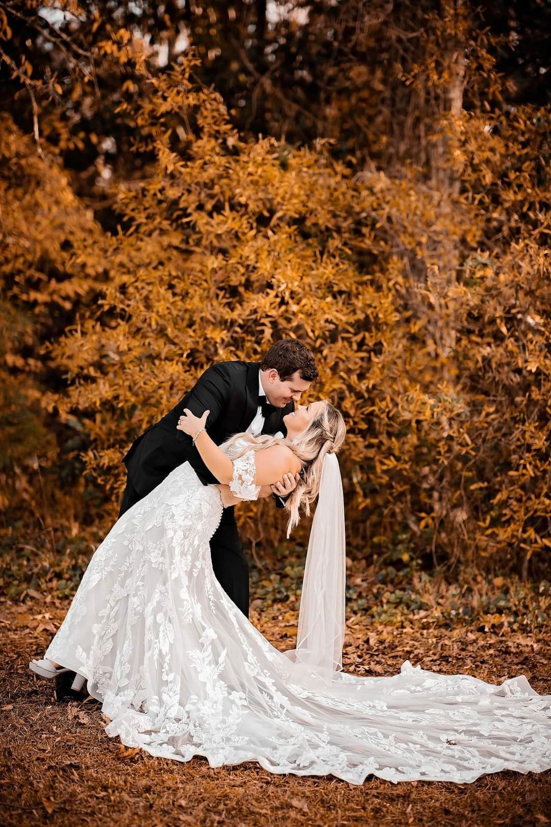 bride and groom kissing in front of fall foliage