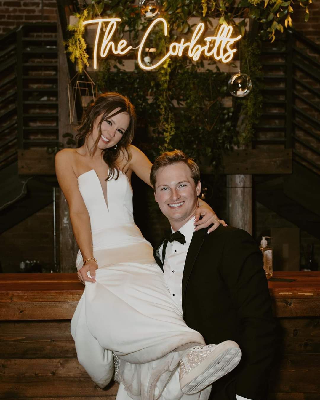 bride and groom smiling in front of custom neon sign