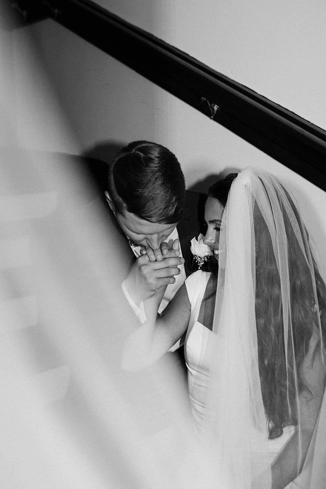 black and white portrait of groom kissing bride's hand