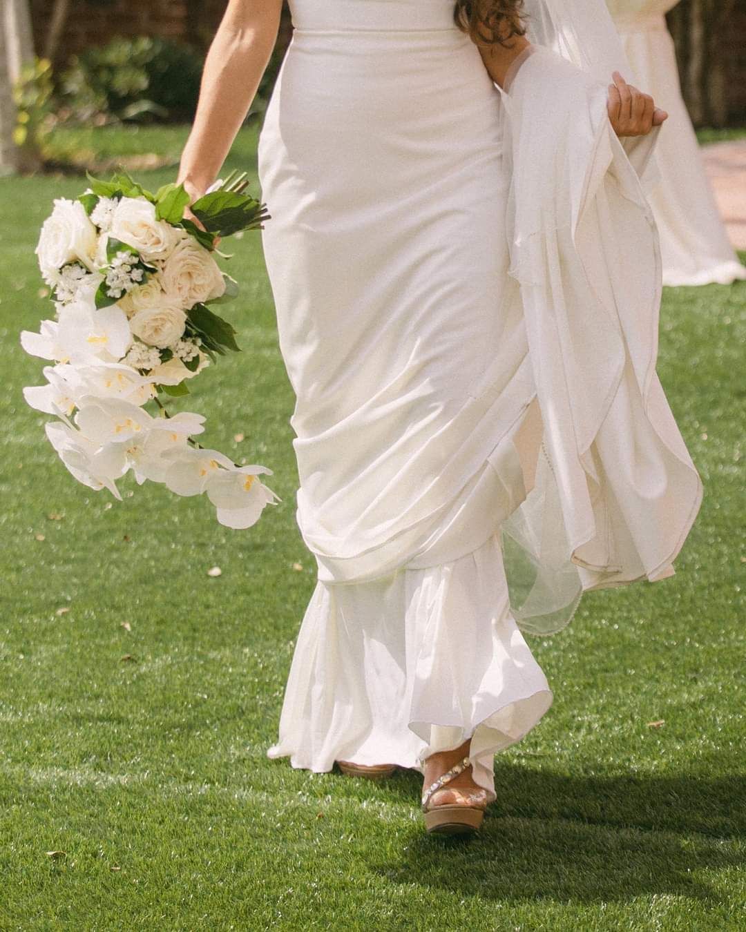 bride walking through lawn holding her veil and train