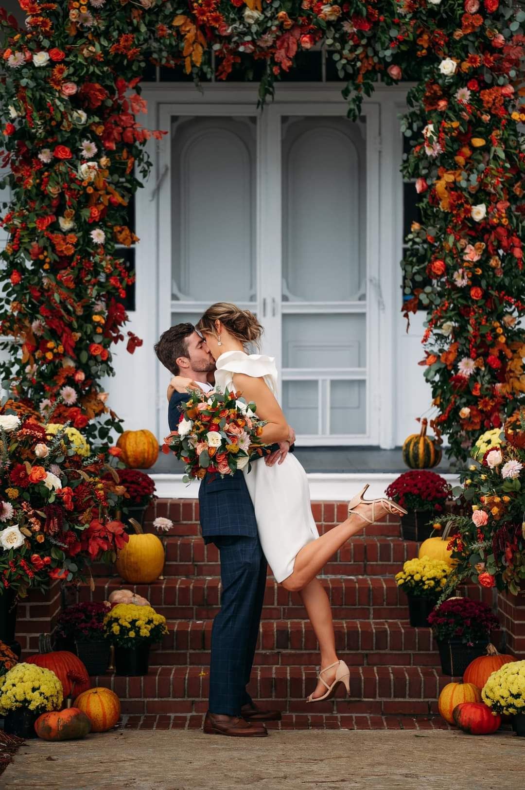 groom lifting and kissing bride in front of large floral arch