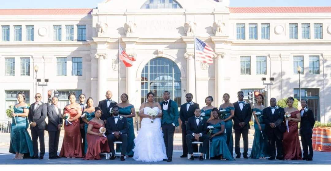 bride and groom with wedding party in front of large venue
