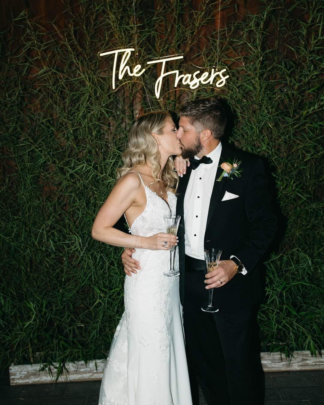 bride and groom kissing in front of neon sign of their name