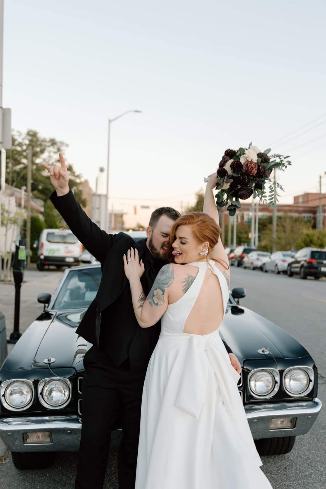 bride and groom cheering in front of black vintage sports car