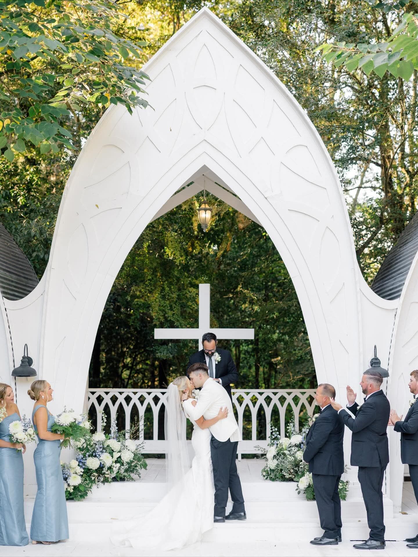 bride and groom kissing during outdoor wedding ceremony under large, ornate arch