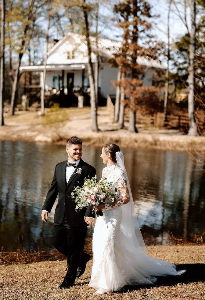 bride and groom walking in front of pond surrounded by fall foliage