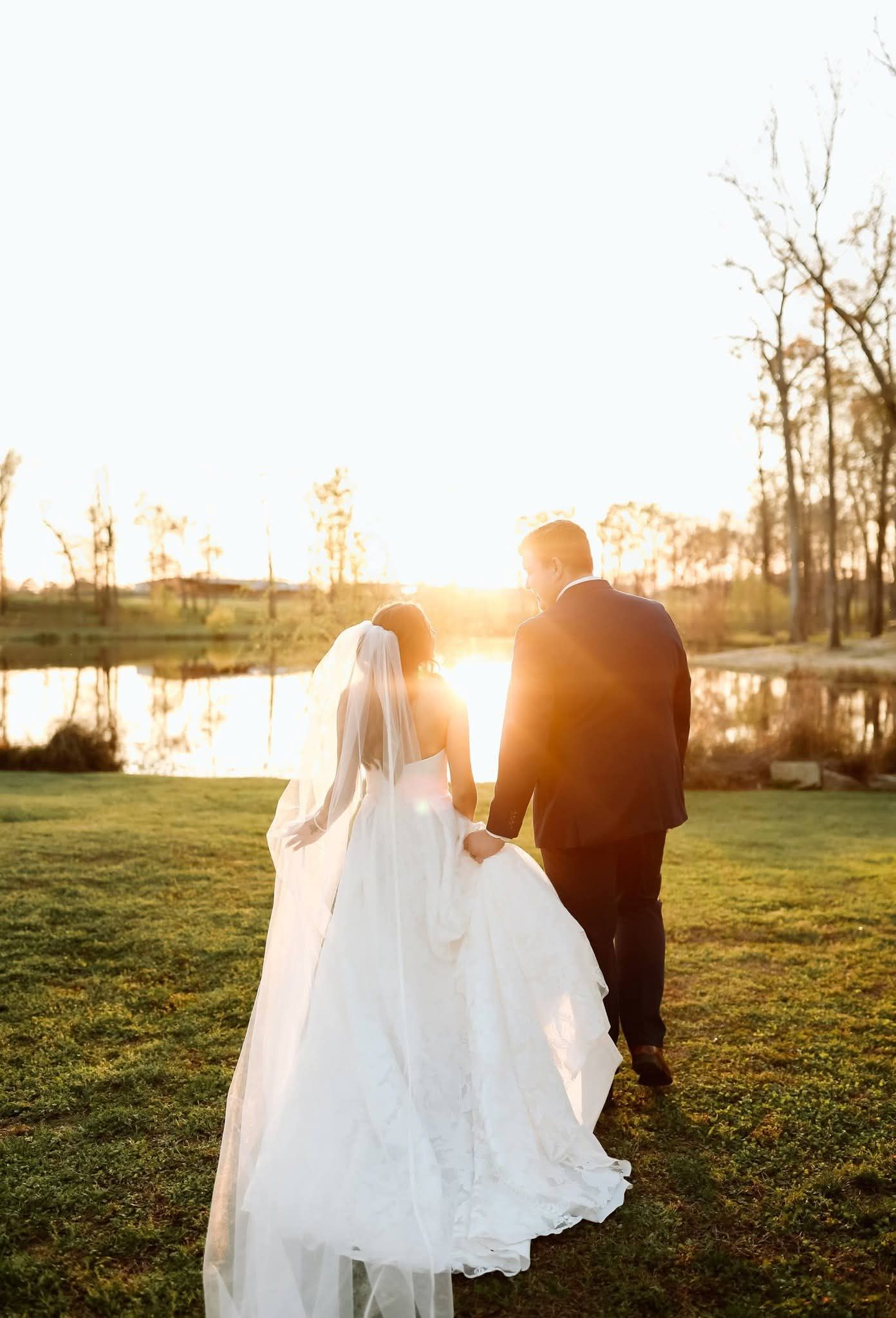 bride and groom walking toward pond at sunset