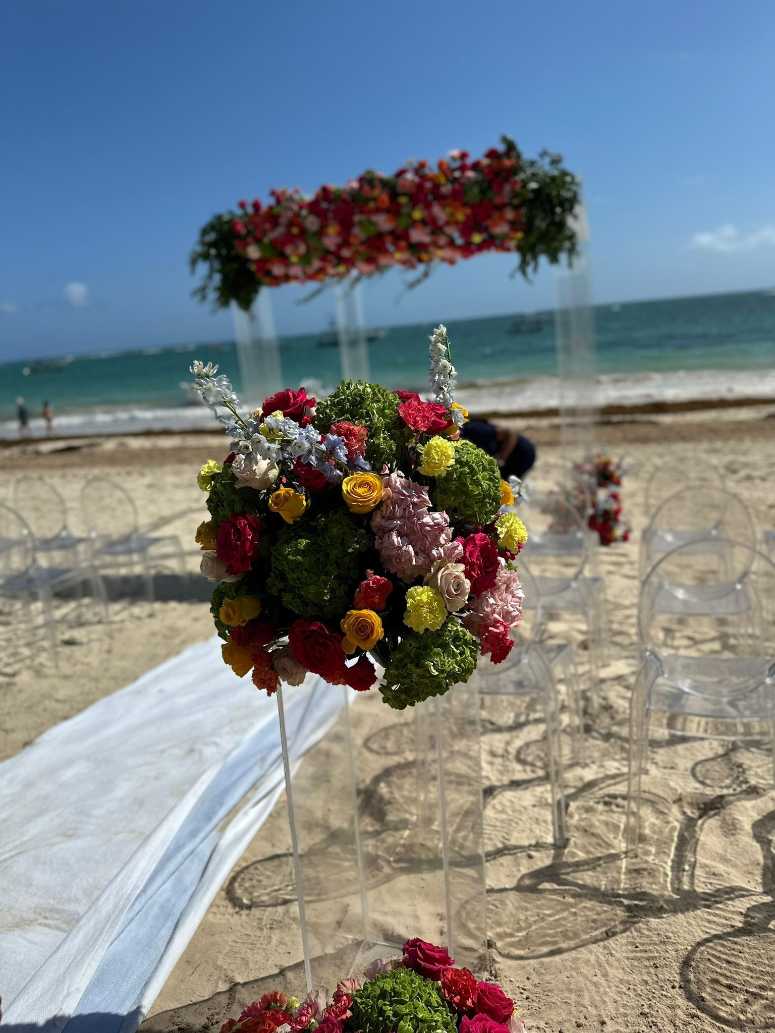 Beach wedding floral arrangement with white ribbons by the ocean, under a clear blue sky