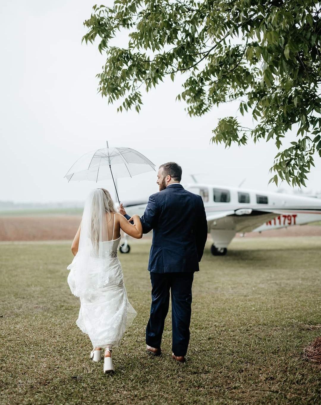 bride and groom walking to private plane under clear umbrella