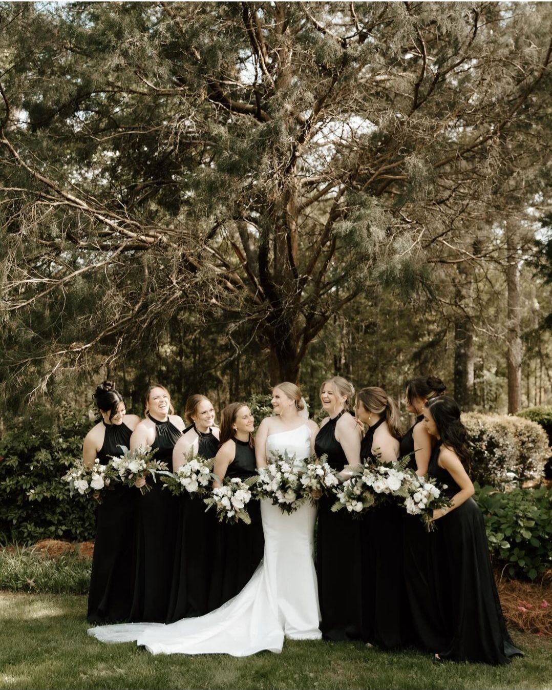 bride surrounded by bridesmaids in black gowns holding white bouquets