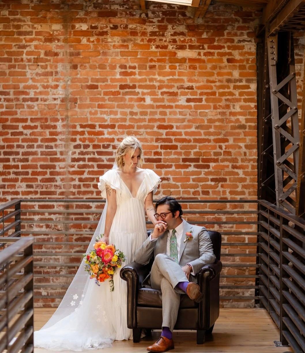 groom sitting in leather chair with bride standing behind