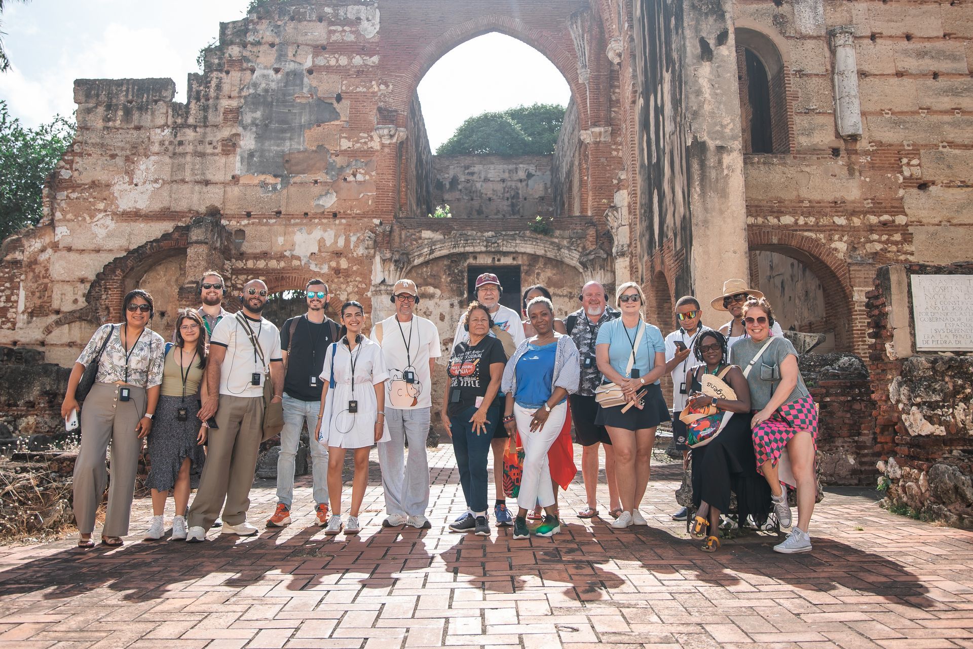 Group of tourists posing in front of a stone ruin with a large archway and brick walkway