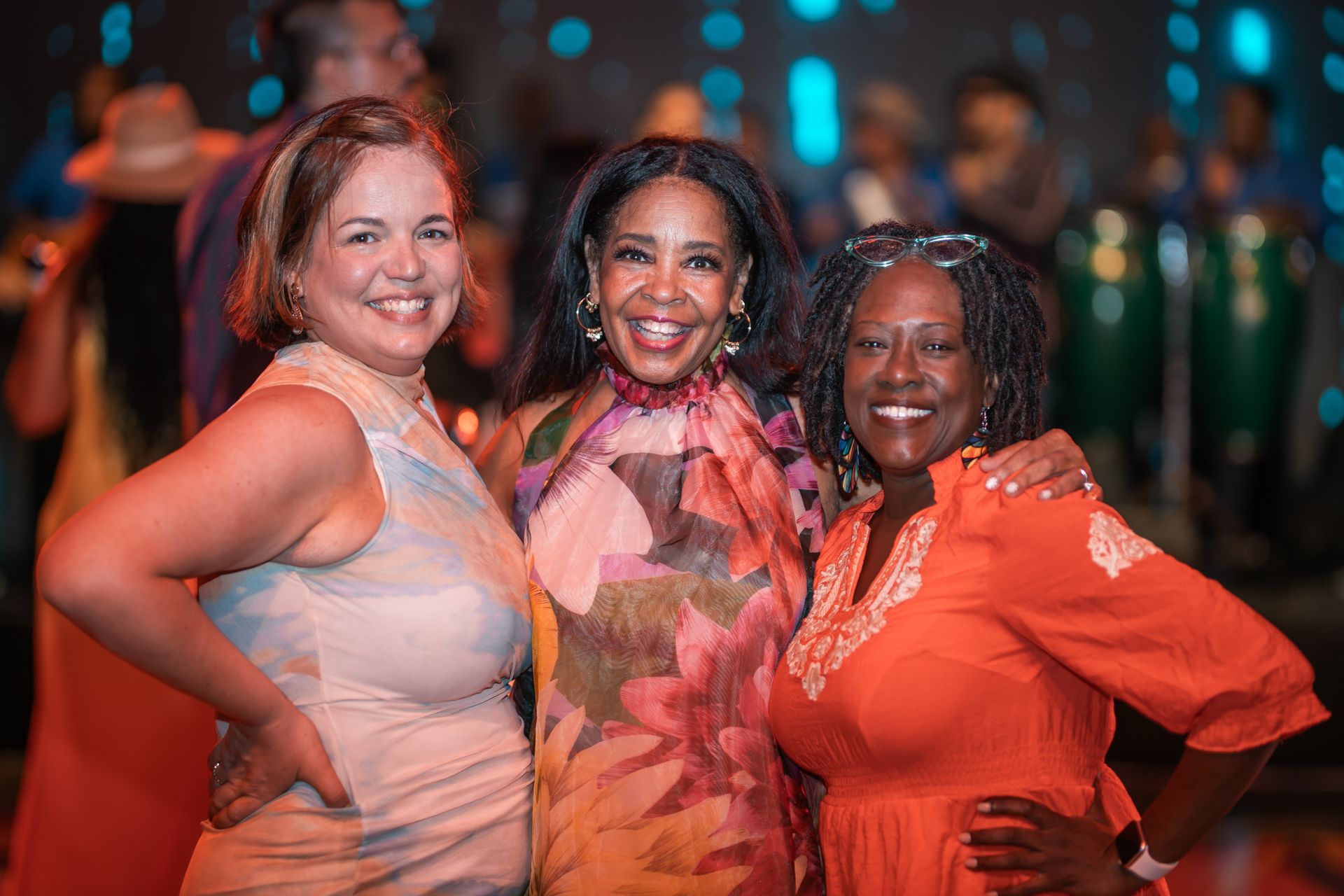 Three people smiling and posing together at a colorful evening event.