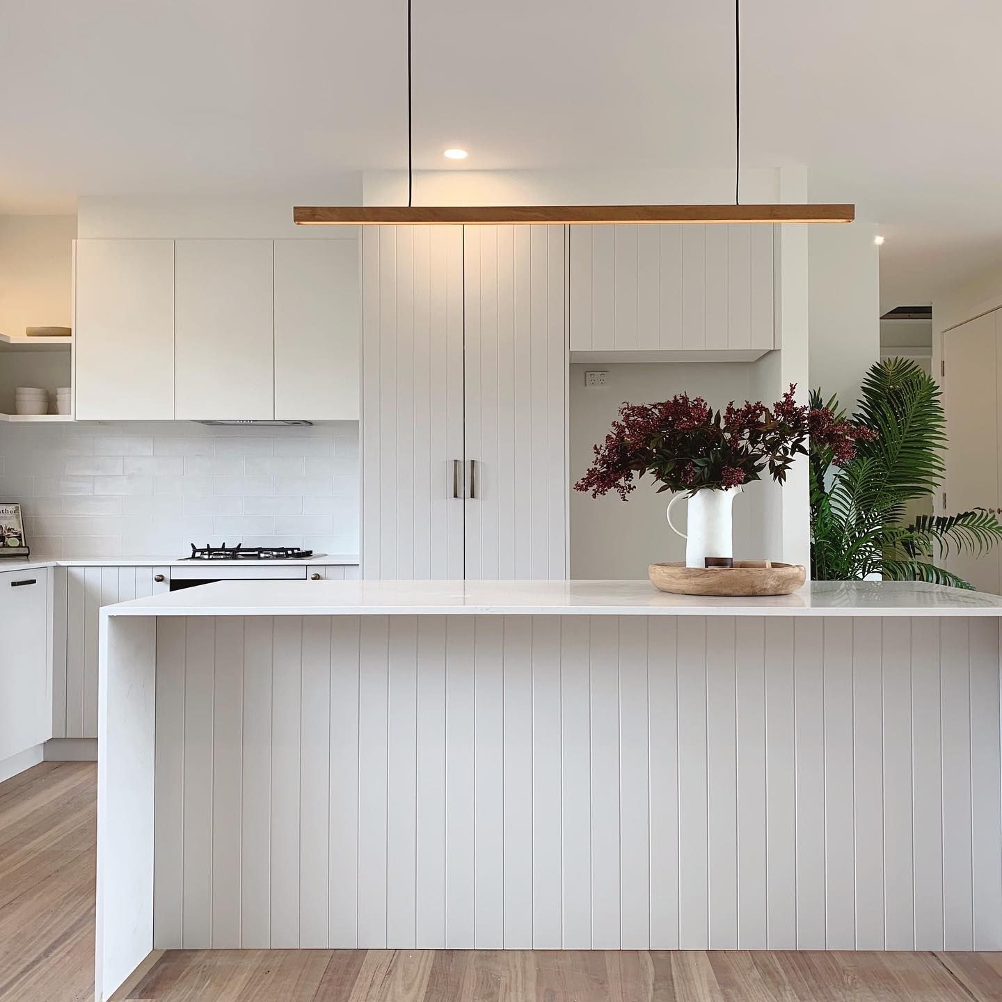 A Kitchen With White Cabinets and a Large Island With a Vase of Flowers on It — Kenross Kitchens In Umina Beach, NSW