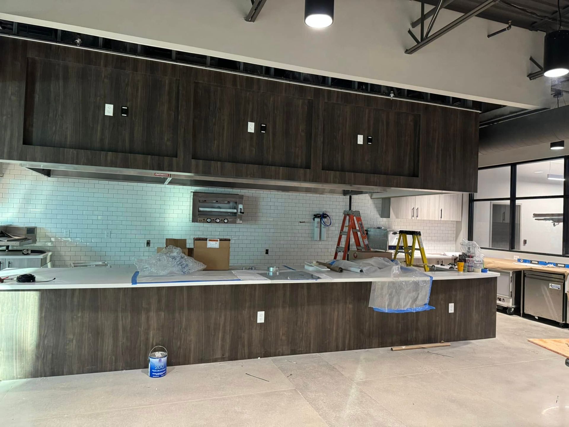 Partially renovated kitchen with dark cabinets, white tile backsplash, and tools on countertops and floor