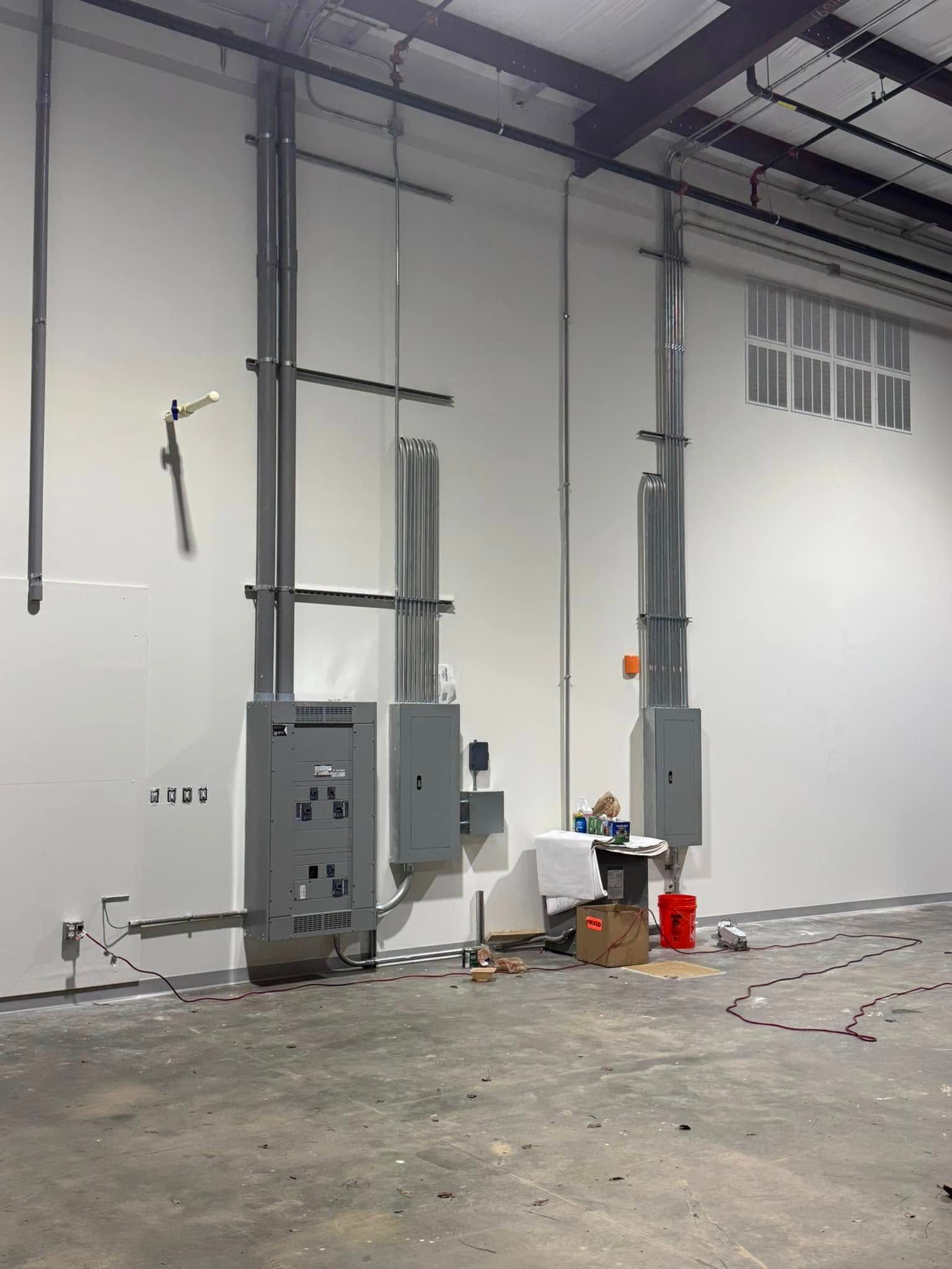 Industrial room with electrical panels, exposed pipes, and scattered tools on a concrete floor