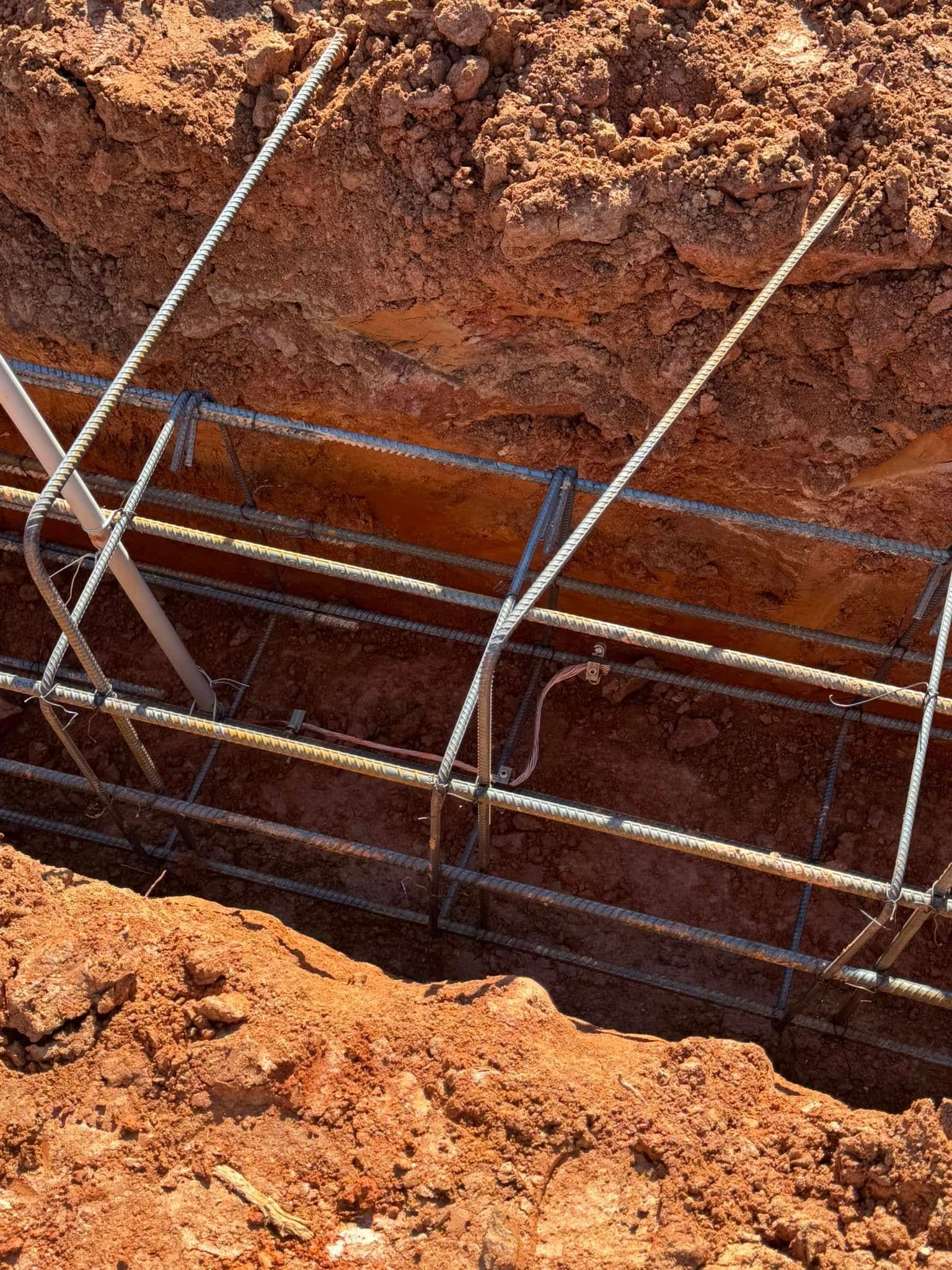 Steel rebar framework in a trench cut into reddish-brown soil at a construction site