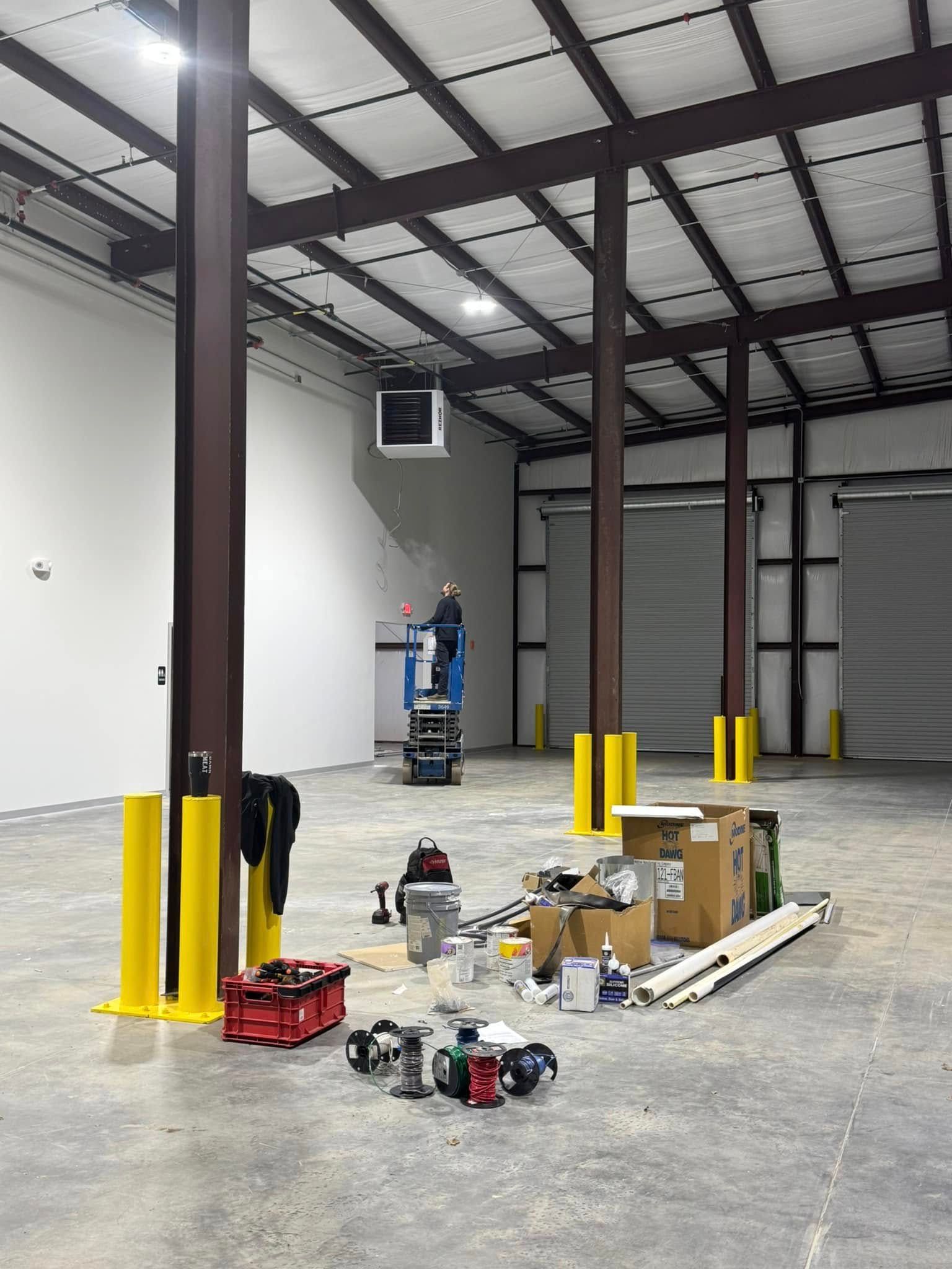 Warehouse interior with steel columns, scattered tools, boxes, and equipment on a concrete floor