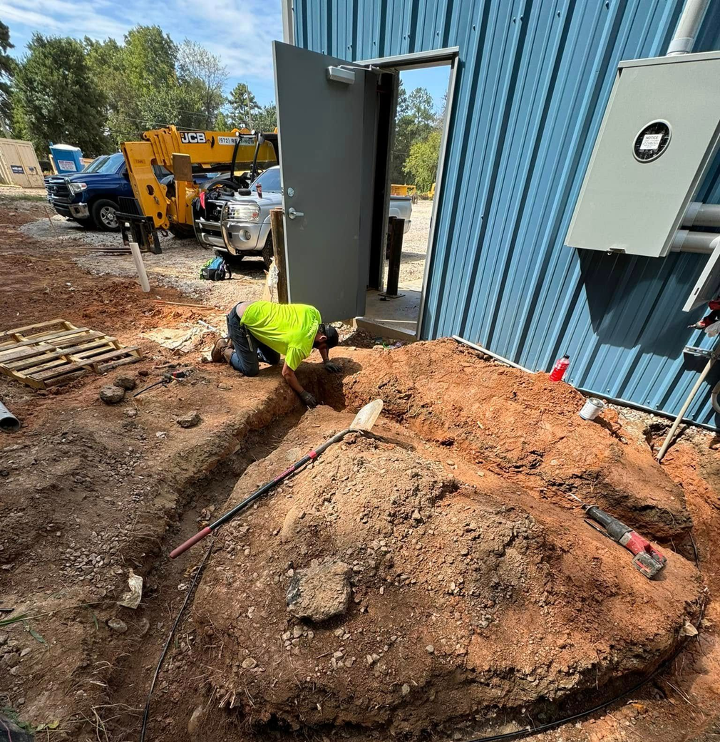 Worker in neon vest digging trench beside blue building at a construction site.
