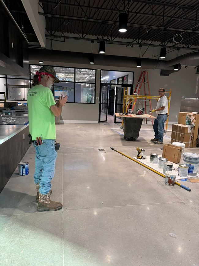 Construction workers in an unfinished office space with tools, boxes, and a ladder.