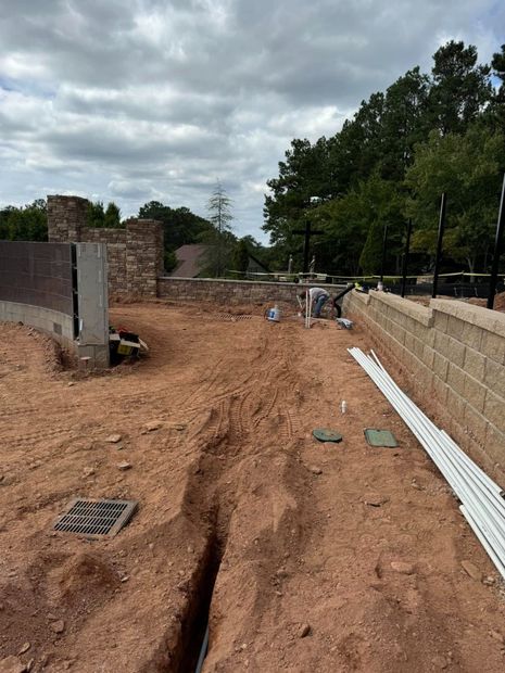 Construction site with dirt trench, concrete walls, stacked materials, and cloudy sky