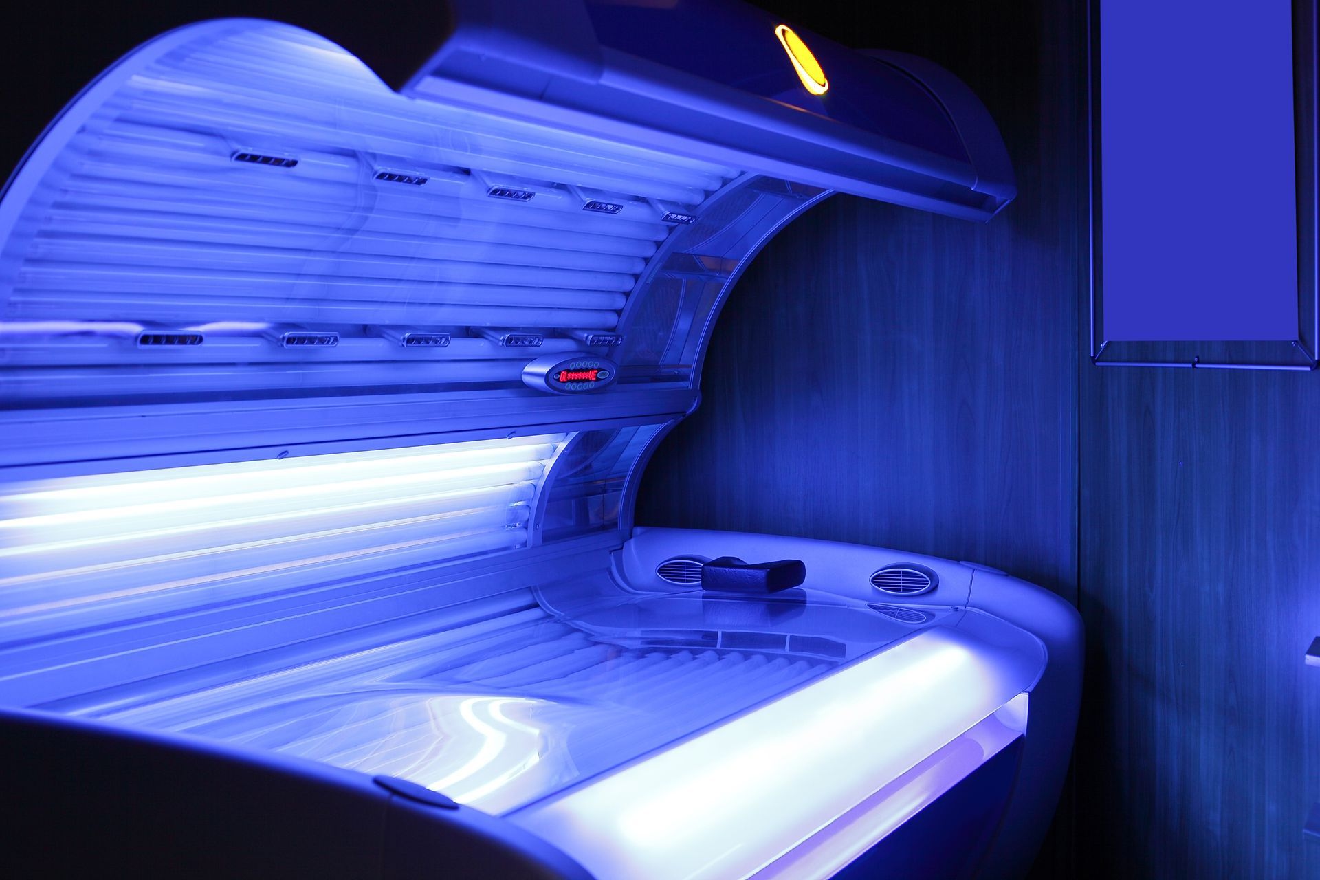 Open tanning bed with bright blue UV lights, indoors.