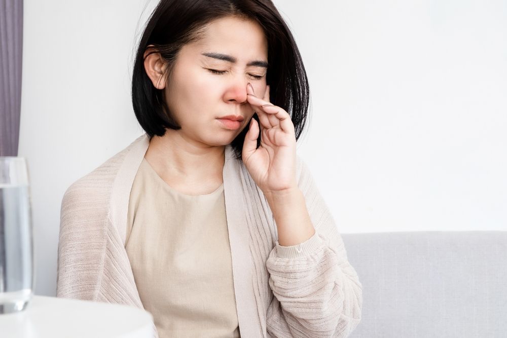 A woman is sitting on a couch holding her nose.