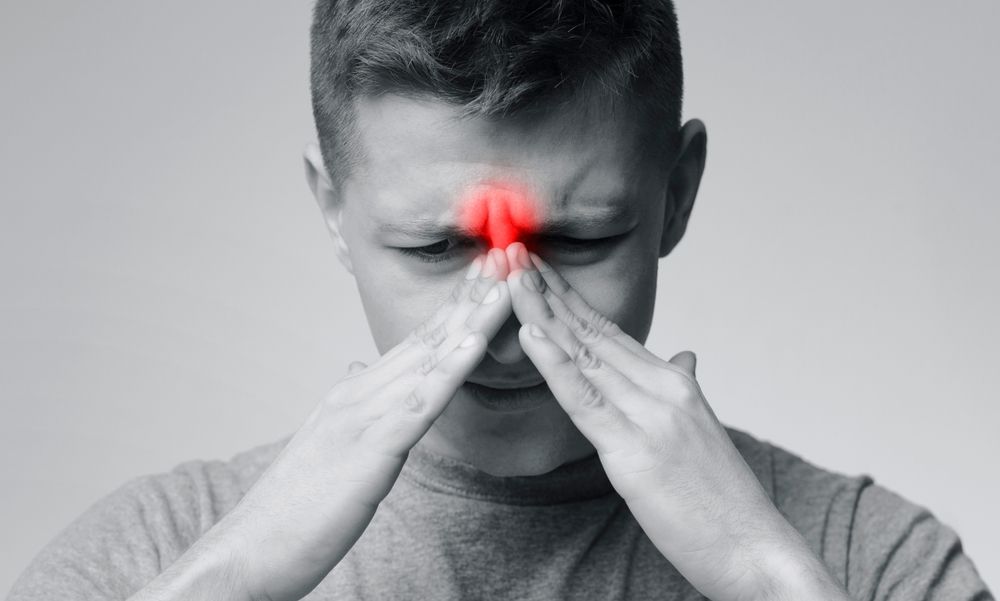 A man is holding his nose in pain because of a sinus infection.