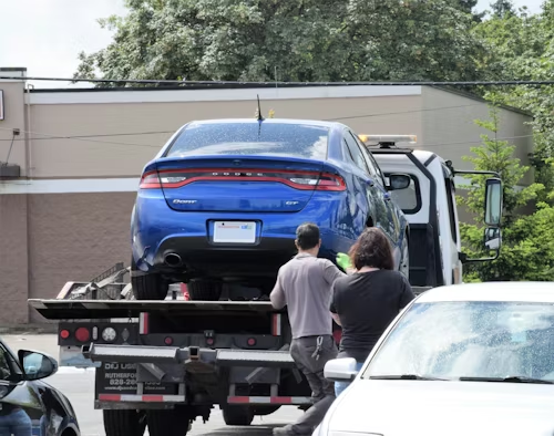 Blue SUV being loaded onto a tow truck while two people stand nearby in a parking lot