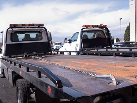 Two white flatbed tow trucks parked outdoors.