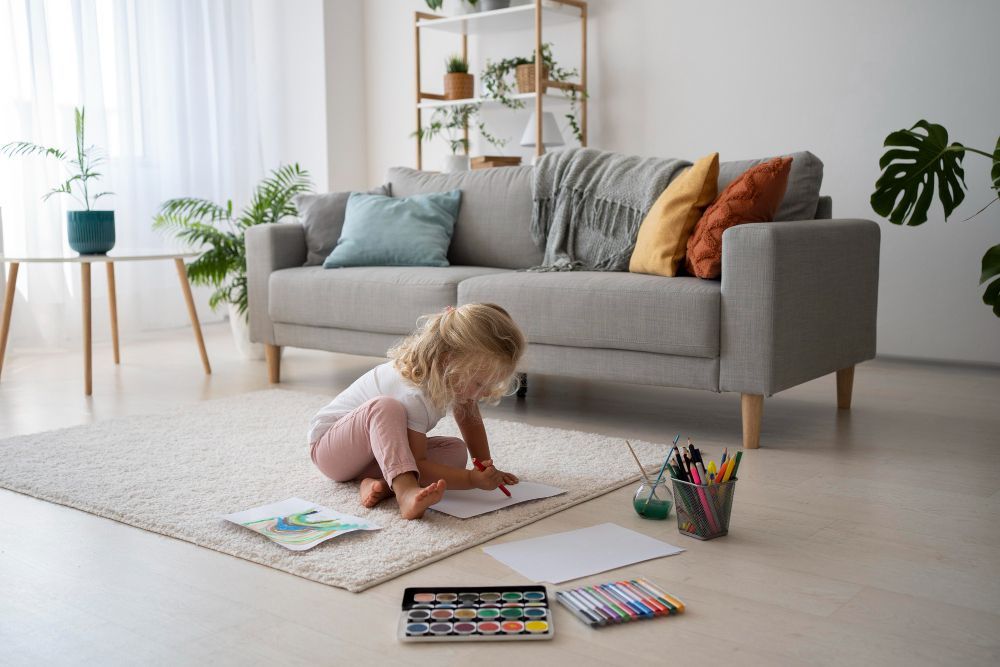Child coloring on the floor in a bright living room, with crayons and a sofa nearby
