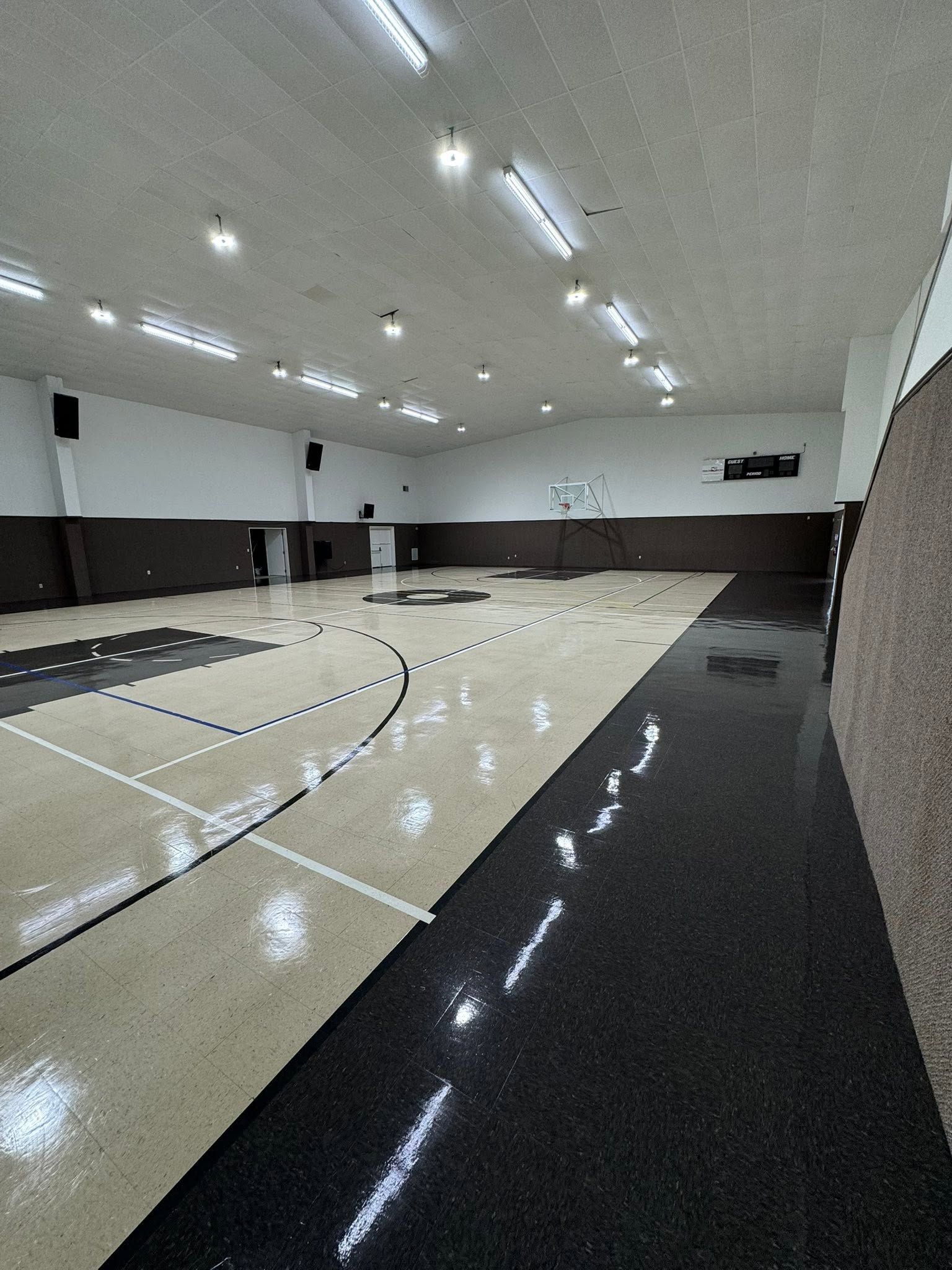 Empty indoor gymnasium with polished black-and-white floor and overhead lights