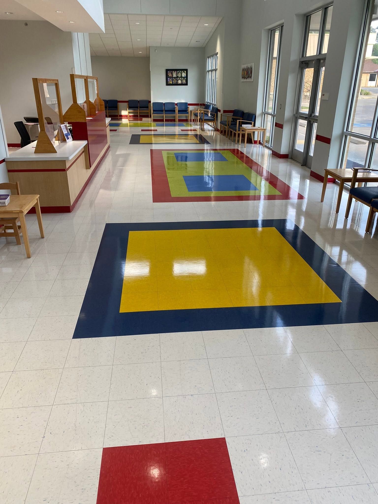 Colorful classroom hallway with red, yellow, and green floor mats and windows along the right side.