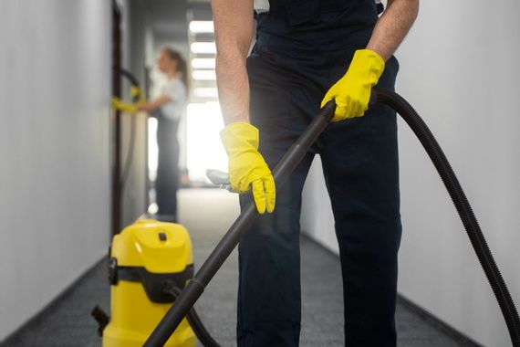 Person vacuuming a hallway carpet with a yellow cleaner while wearing yellow gloves