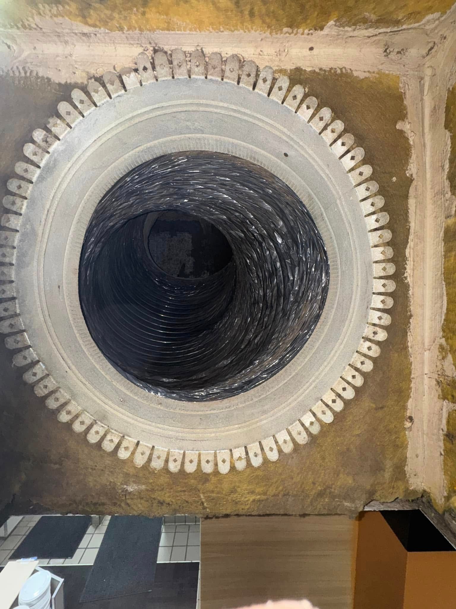 Top-down view of a large circular manhole opening set in concrete, with a dark shaft inside.