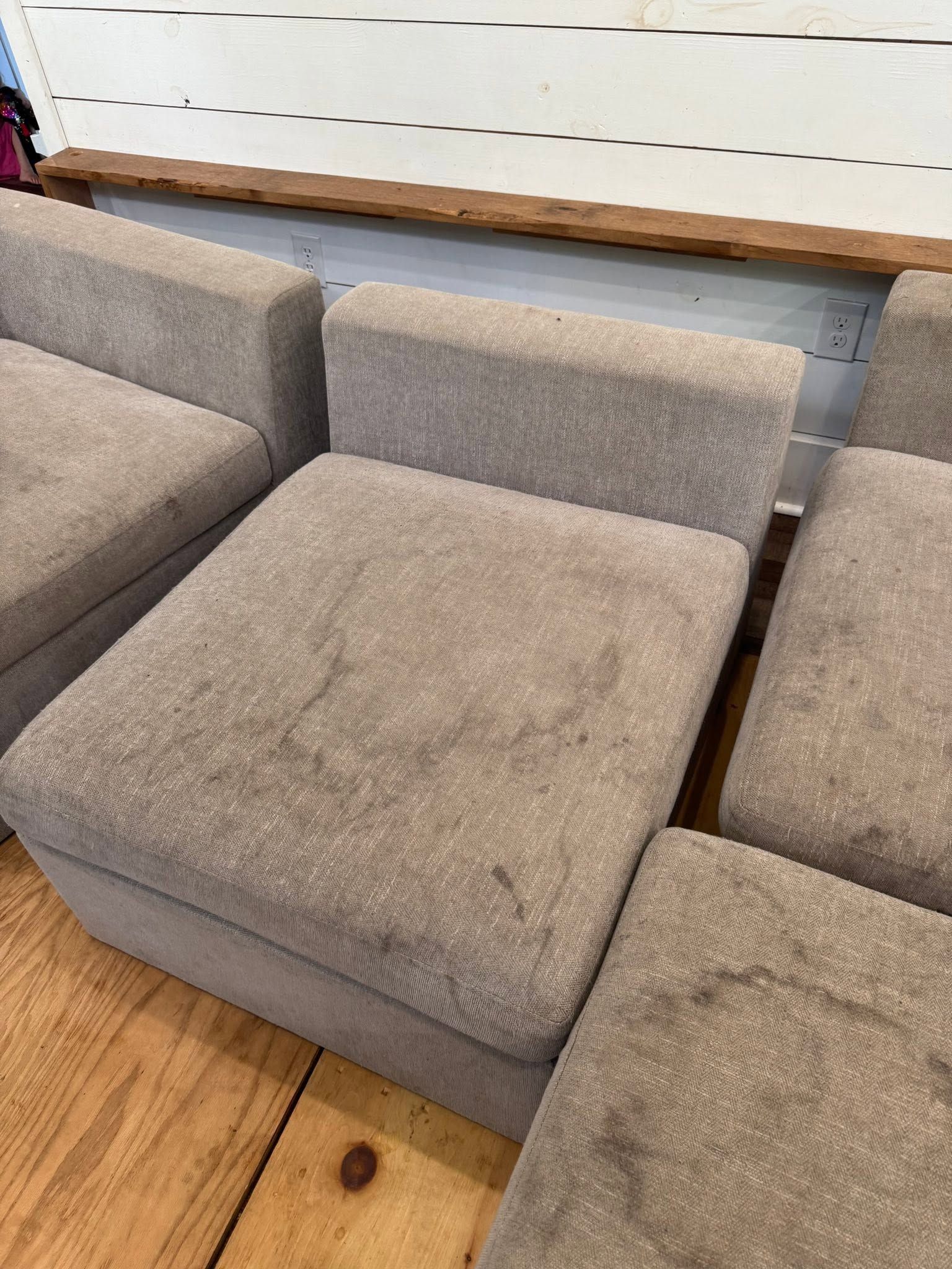 Gray upholstered sectional sofa with cushioned seats in a room with a wood floor and white wall shelves